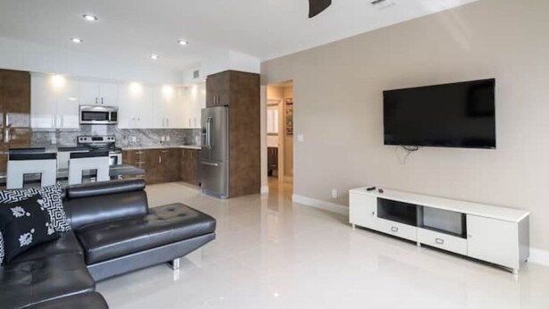 Una sala de estar moderna con un sofá de cuero negro, un televisor de pantalla plana montado en la pared y un mueble blanco para equipo de entretenimiento.
