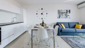 A modern kitchen with white cabinets, a dining table set for four, and a blue sofa with yellow cushions in the living area. - Holiday apartment mit Meerblick (Crikvenica)