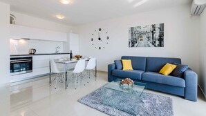 A modern living room with a blue sofa, a glass coffee table, and a dining area with a white table and chairs. - Holiday apartment mit Meerblick (Crikvenica)