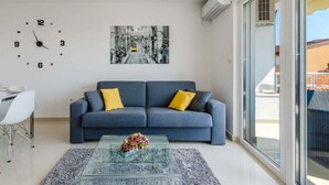 A modern living room with a sofa, a glass coffee table, a wall clock, and a large window. - Holiday apartment mit Meerblick (Crikvenica)