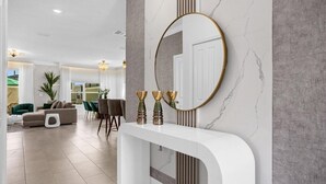 A modern living room with a white console table, a large mirror, and a green sofa. - 5 Bedroom/ 4 Bathroom/ Storey Lake (2689SS) (Kissimmee)