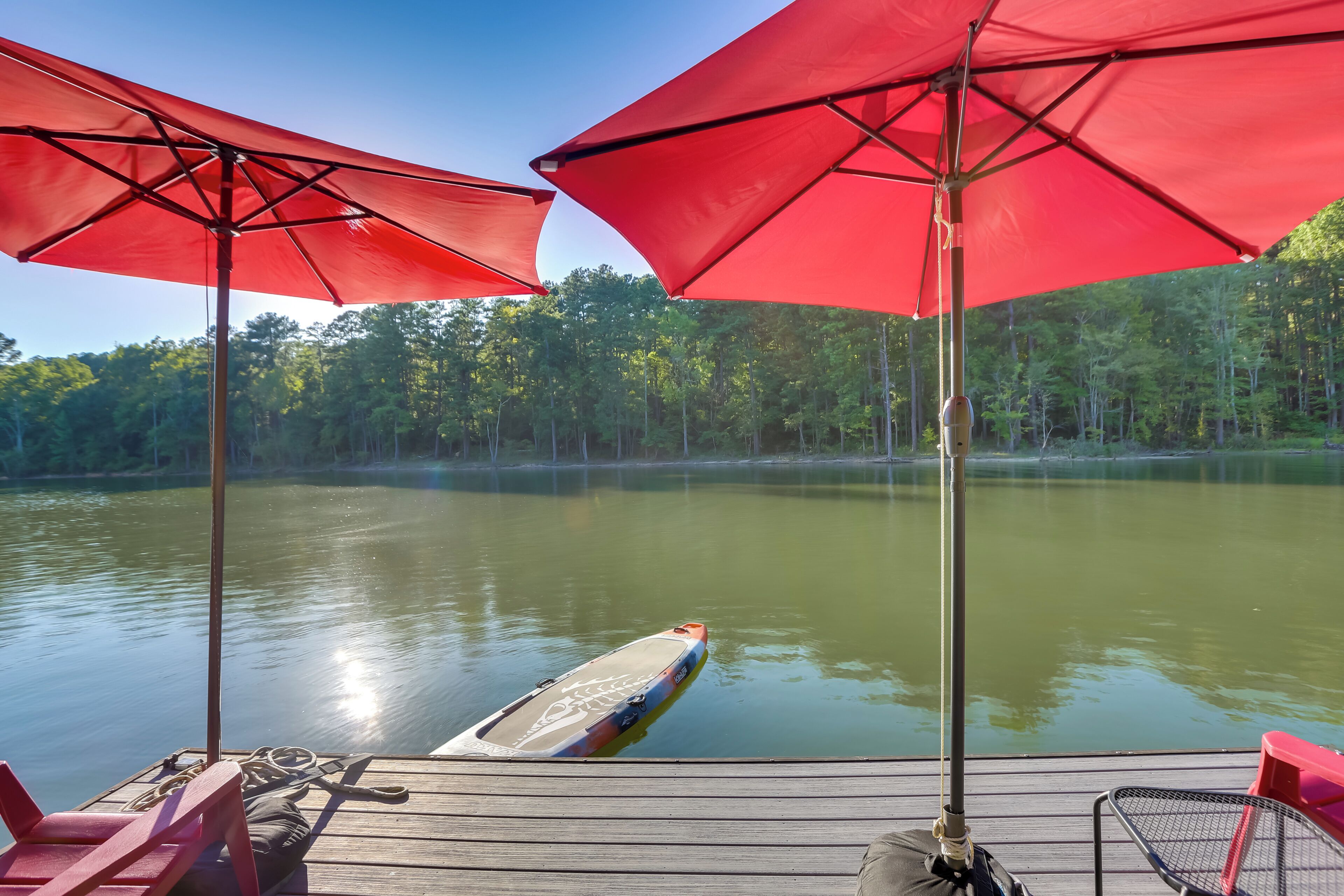 A wooden dock with red umbrellas and a paddleboard in the water.