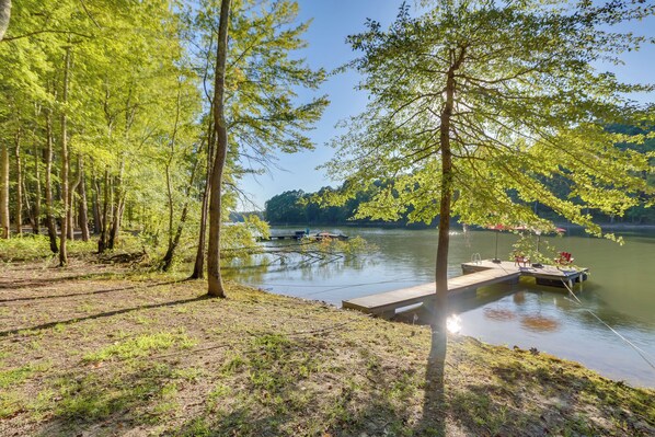 A lakeside dock with a wooden platform and chairs, surrounded by trees and a clear sky.