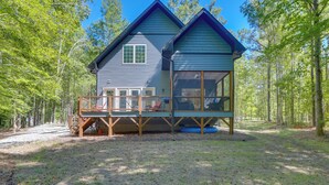 A two-story cabin with a deck, surrounded by trees.