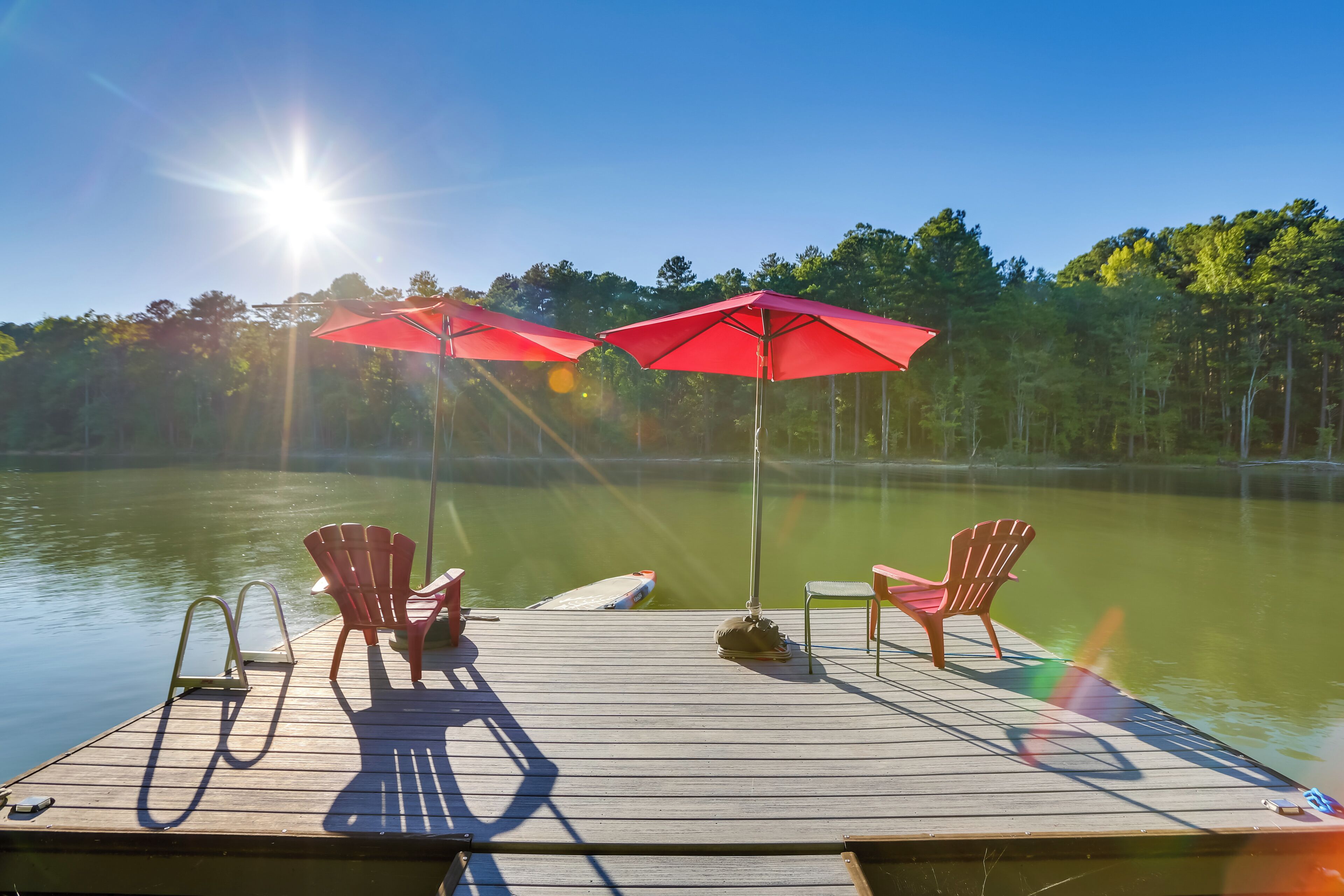 Une jetée en bois, agrémentée de deux parasols rouges et de deux fauteuils Adirondack, au bord d’un lac paisible.