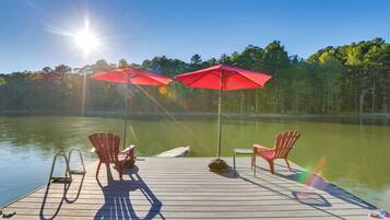 Une jetée en bois, agrémentée de deux parasols rouges et de deux fauteuils Adirondack, au bord d’un lac paisible.