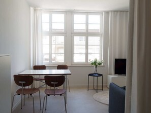 Een kamer met een eettafel en stoelen, een bijzettafeltje met een plant, een televisie en een bank.