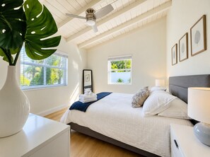 A bedroom with a bed, bedside table, lamp, and a large plant.