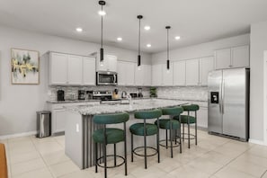 Una cocina moderna con gabinetes blancos, un refrigerador de acero inoxidable, un microondas integrado y una encimera de granito.