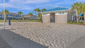Un hotel frente a la playa con zona de piscina techada, una red de voleibol y palmeras al fondo.