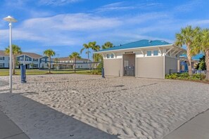 Un hôtel situé en bord de mer, doté d’une piscine couverte, d’un filet de volley-ball et de palmiers en arrière-plan.