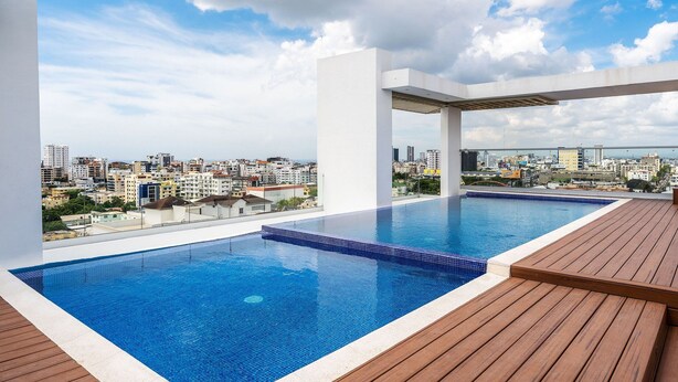 Una piscina infinita en la azotea con terraza de madera y vista a la ciudad.