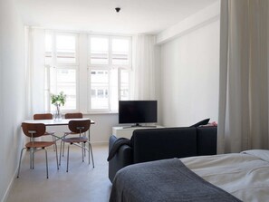 Een hotelkamer met een bed, een bureau met televisie, een stoel en een raam met gordijnen.