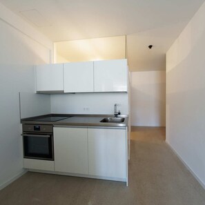 Een kleine keuken met witte kasten, een ingebouwde oven en een roestvrijstalen spoelbak.
