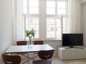 Een moderne kamer met een eettafel, stoelen, een televisie op een kast en een raam met gordijnen.