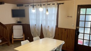 Ein Essbereich mit einem Holztisch, weißen Stühlen, einem an der Wand befestigten Fernseher und einer Tür mit satinierten Glasfeldern.