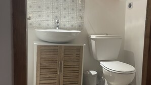 Ein Badezimmer mit Holzschrank, Waschbecken, Toilette und Fliesenrückwand.