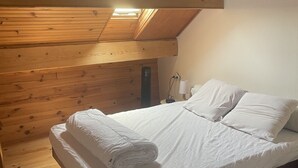 Ein Zimmer aus Holz mit einem Bett, einem Fenster und einer Pendelleuchte.