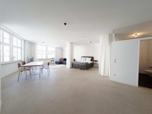 Een ruime kamer met een grote tafel en stoelen, een bed, en een apart gedeelte met een wastafel en toilet.