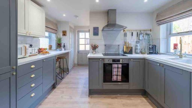 A modern kitchen with grey cabinets, a central island, and a built-in oven. - Tranquil Appleby House Retreat (Appleby-in-Westmorland)