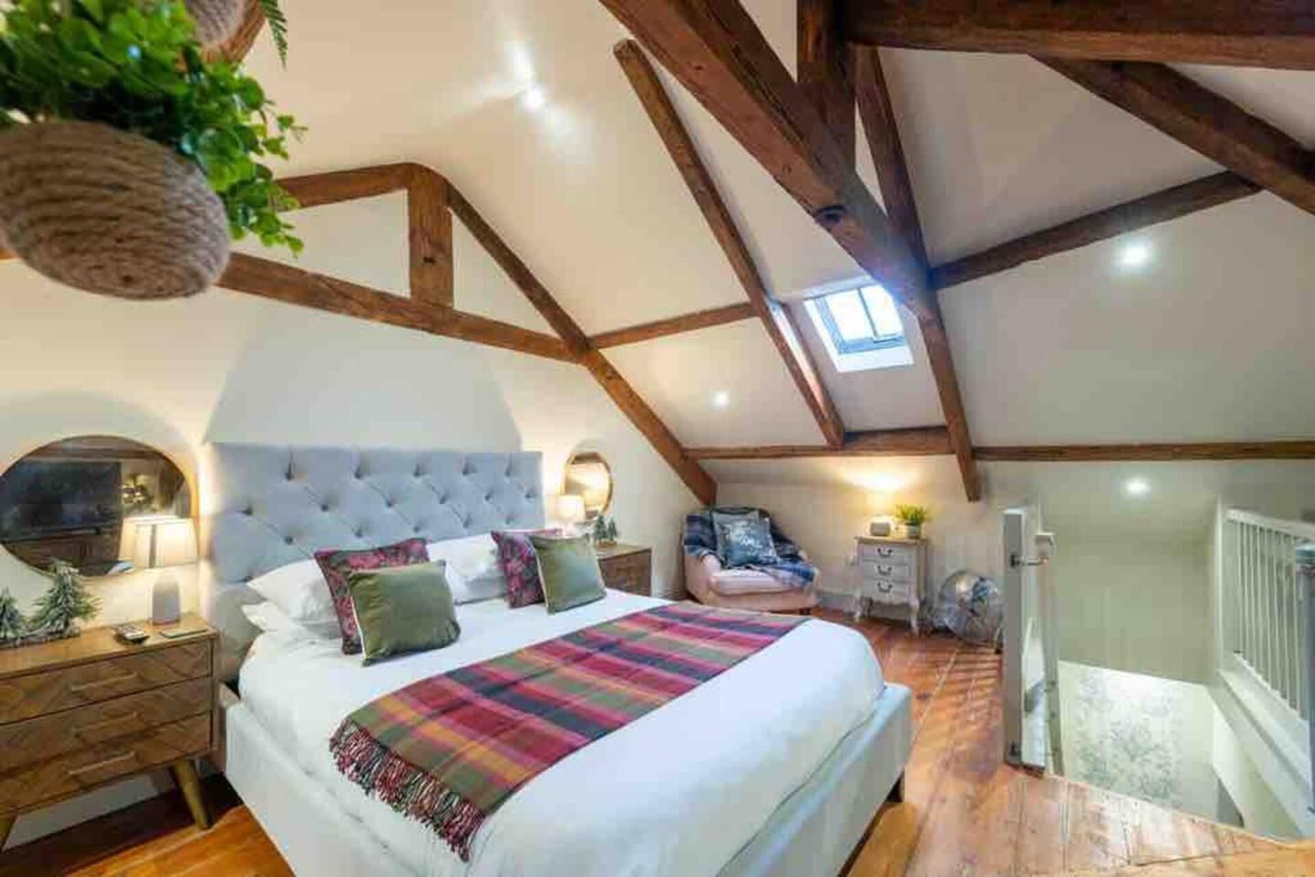 A bedroom with a large bed, wooden beams, a skylight, and a small table with a plant.