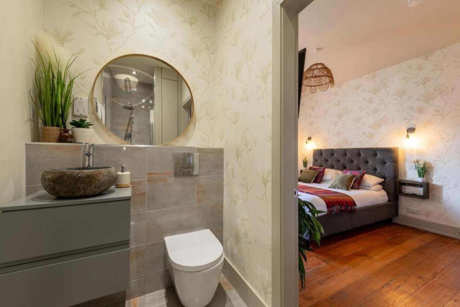 A modern bathroom with a round mirror, a stone sink, and a toilet.