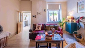 A cozy living room with a sofa, a coffee table with a candle, and a window with a view of trees. - Tranquil Appleby House Retreat (Appleby-in-Westmorland)