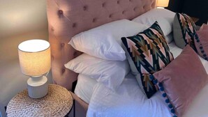 A neatly made bed with white and patterned pillows, a round woven side table with a lamp, and a tufted headboard. - Inviting 2-bed House in Sunderland, Wifi, Parking (Sunderland)