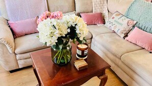 A wooden coffee table with a vase of flowers and a candle in a living room with a beige sofa and pink cushions. - Inviting 2-bed House in Sunderland, Wifi, Parking (Sunderland)