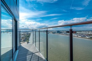 A high-rise building with a balcony overlooking a river and cityscape.