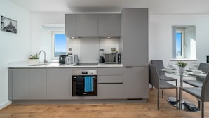 A modern kitchen with grey cabinetry, a built-in oven, and a dining area with a glass table and grey chairs.