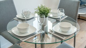 A modern dining table with glass top, surrounded by grey upholstered chairs.