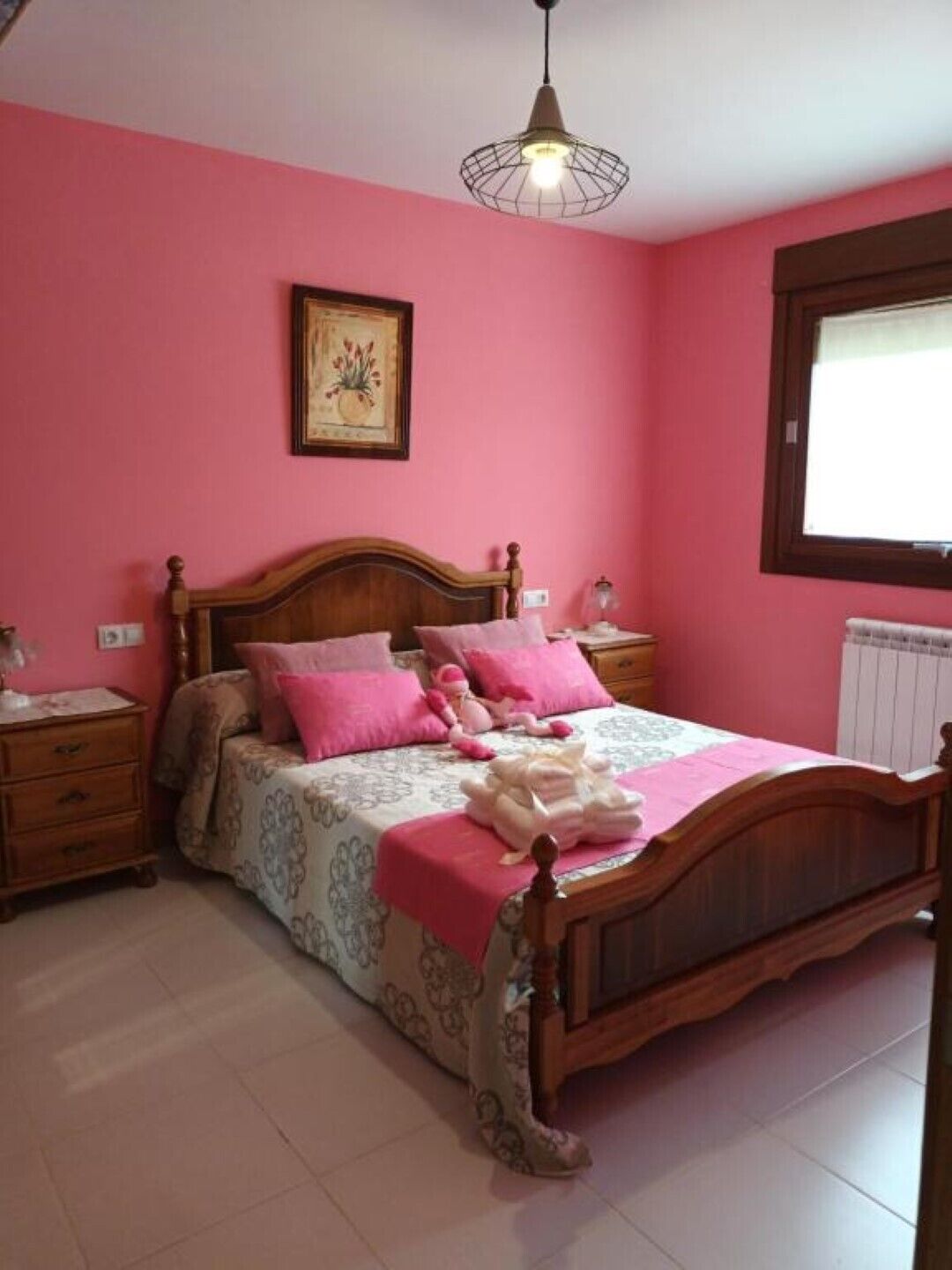Een slaapkamer met een houten bed, roze wanden en een hanglamp.