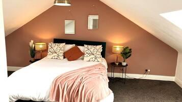 A bedroom with a sloped ceiling, a bed with a pink blanket, two bedside lamps, and two wall-mounted mirrors.