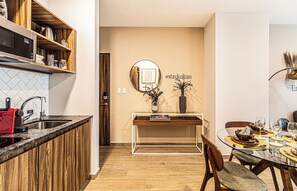A modern kitchen with a microwave, stove, and red appliance on the counter. There is a dining area with a glass table, chairs, and a vase with dried plants. - Kukun Tonalá 30 Roma (Mexico City)