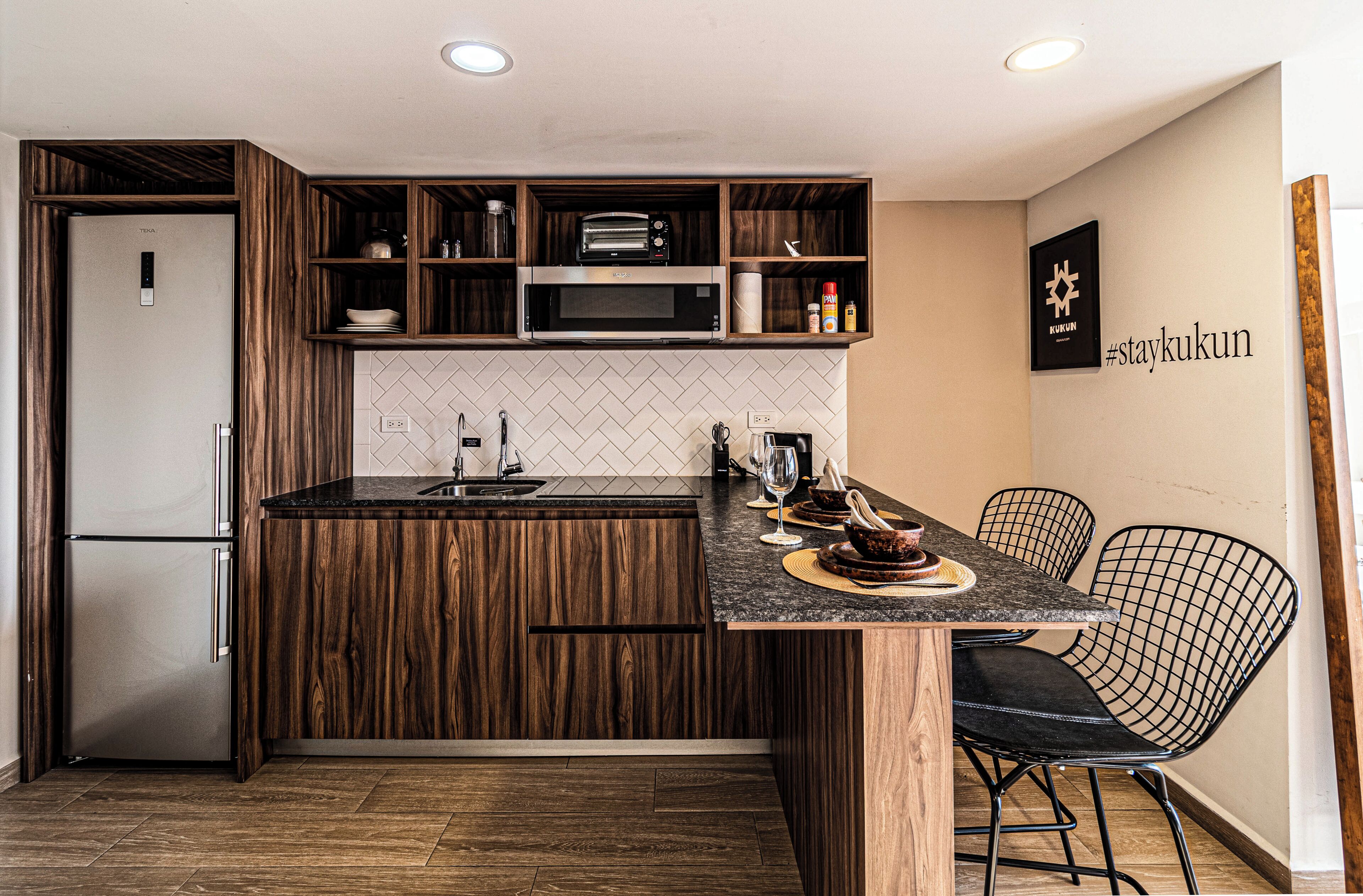 A modern kitchen with wooden cabinetry, a built-in microwave, and a dining area with wire chairs.