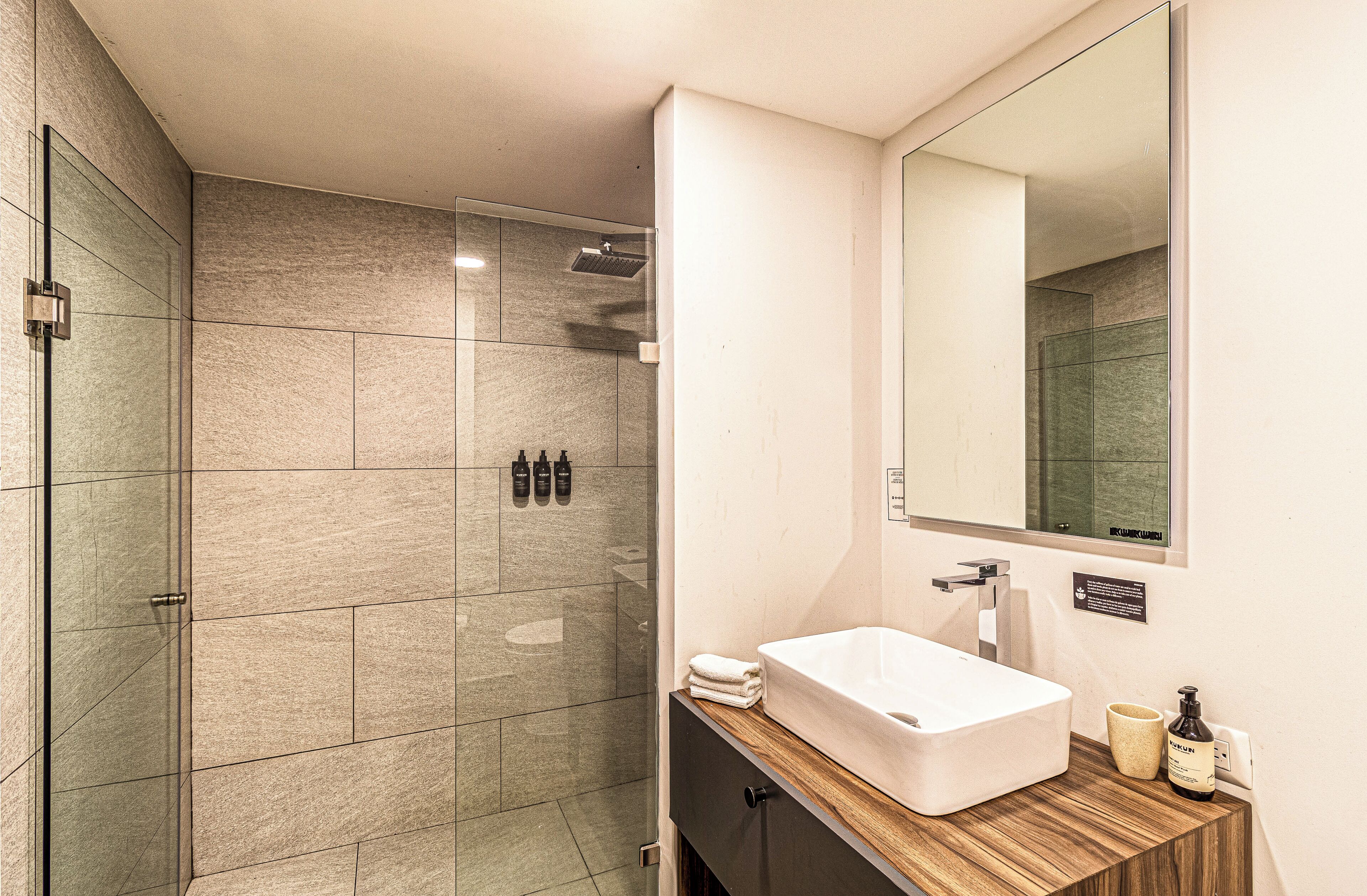 A modern bathroom with a glass shower enclosure, a wooden vanity with a sink, and a large mirror.
