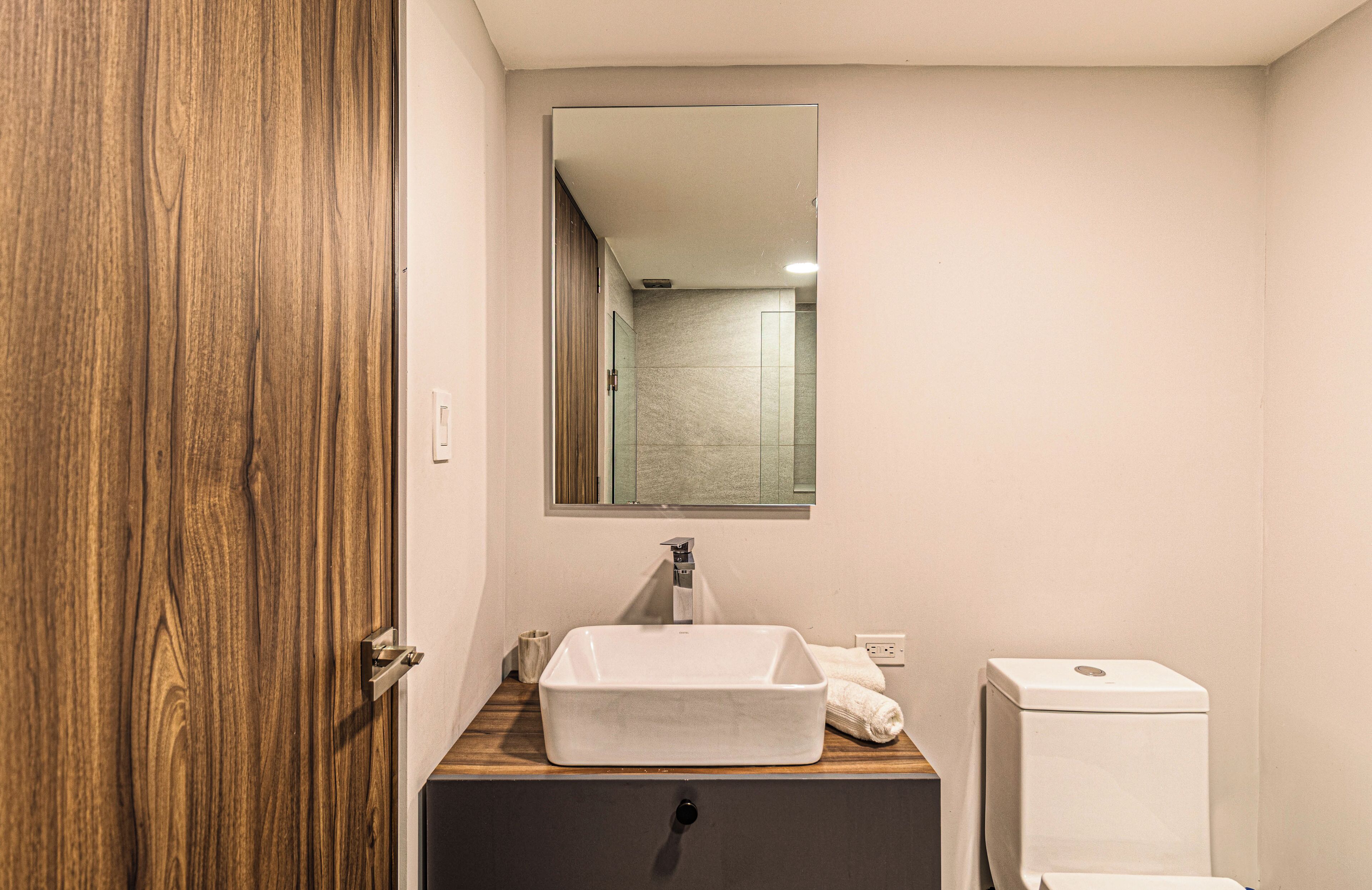 Une salle de bain avec une porte en bois, un lavabo blanc, un miroir et des toilettes.