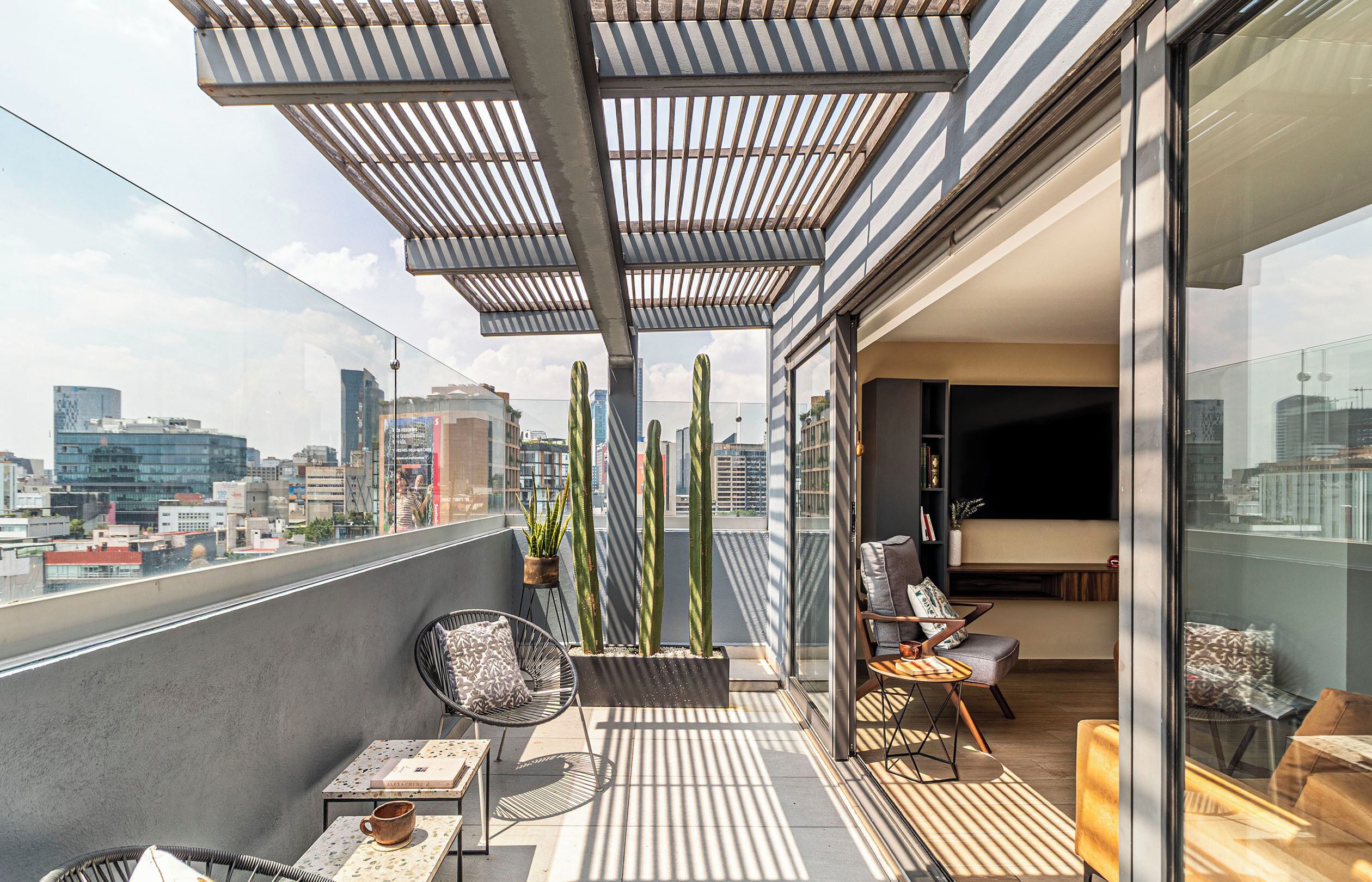 Varanda moderna com vista para a cidade, com área de estar, cadeiras, mesa, plantas em vasos e porta de vidro que dá para um espaço interior.