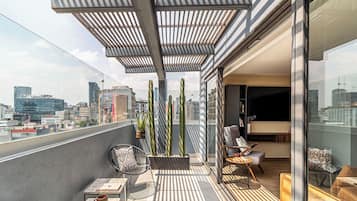 Varanda moderna com vista para a cidade, com área de estar, cadeiras, mesa, plantas em vasos e porta de vidro que dá para um espaço interior.