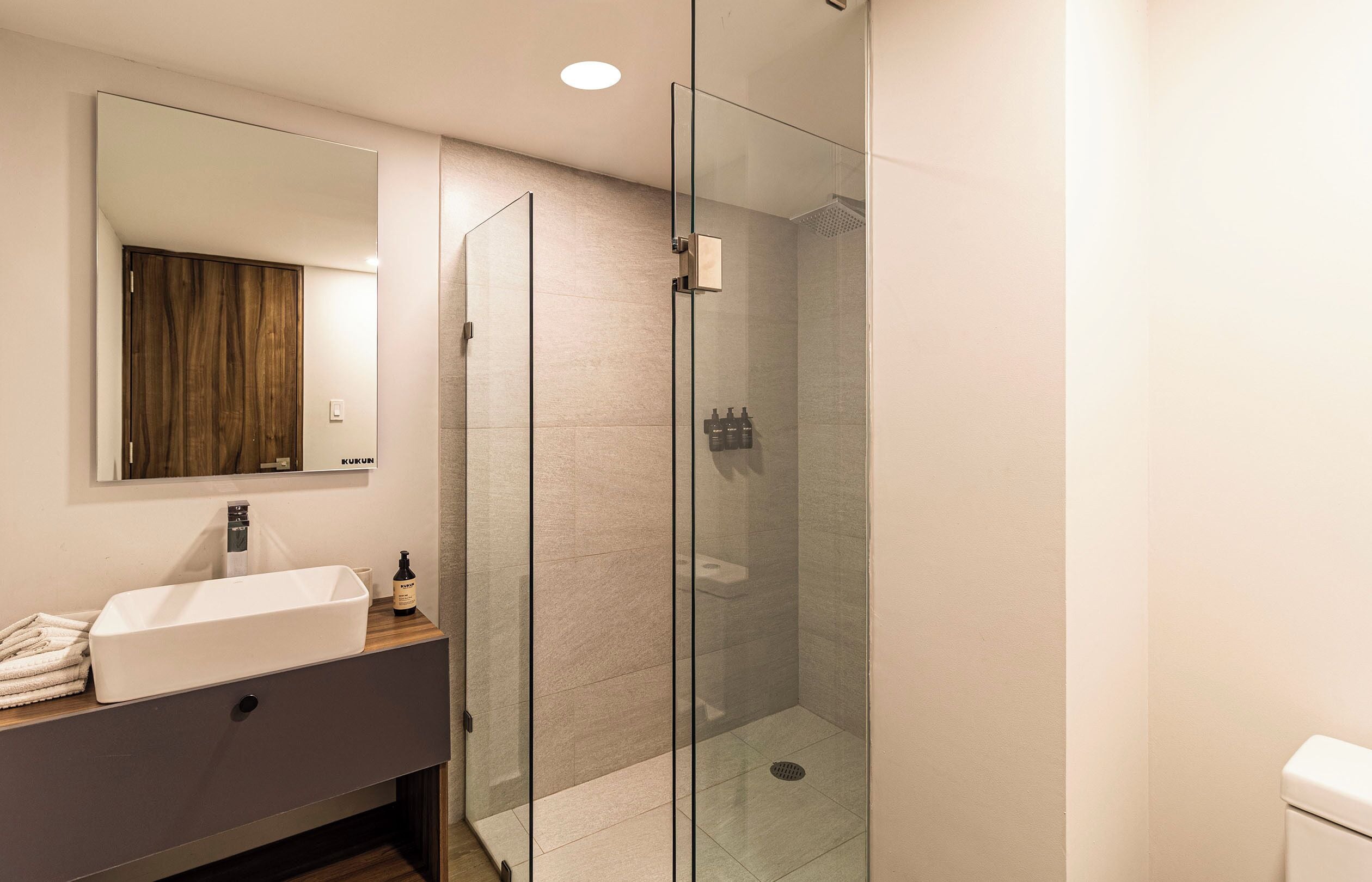 A modern bathroom with a glass-enclosed shower, a white sink, and a mirror above it.