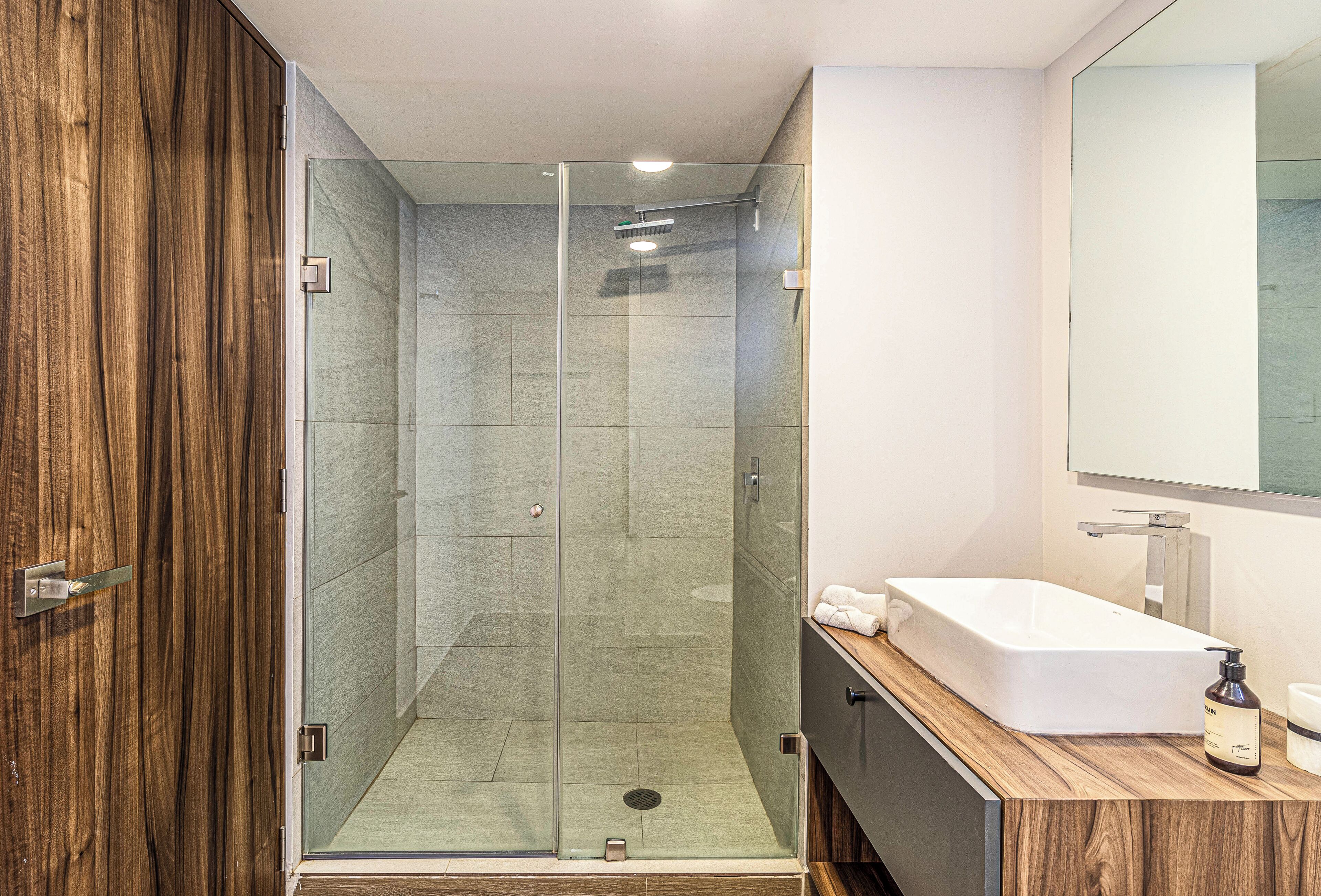 A modern bathroom with a glass-enclosed shower, a wooden vanity, and a large mirror.