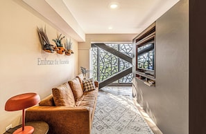 Un interior moderno con un sofá, un taburete rojo, un arreglo de plantas en la pared y una escalera que lleva a un balcón.