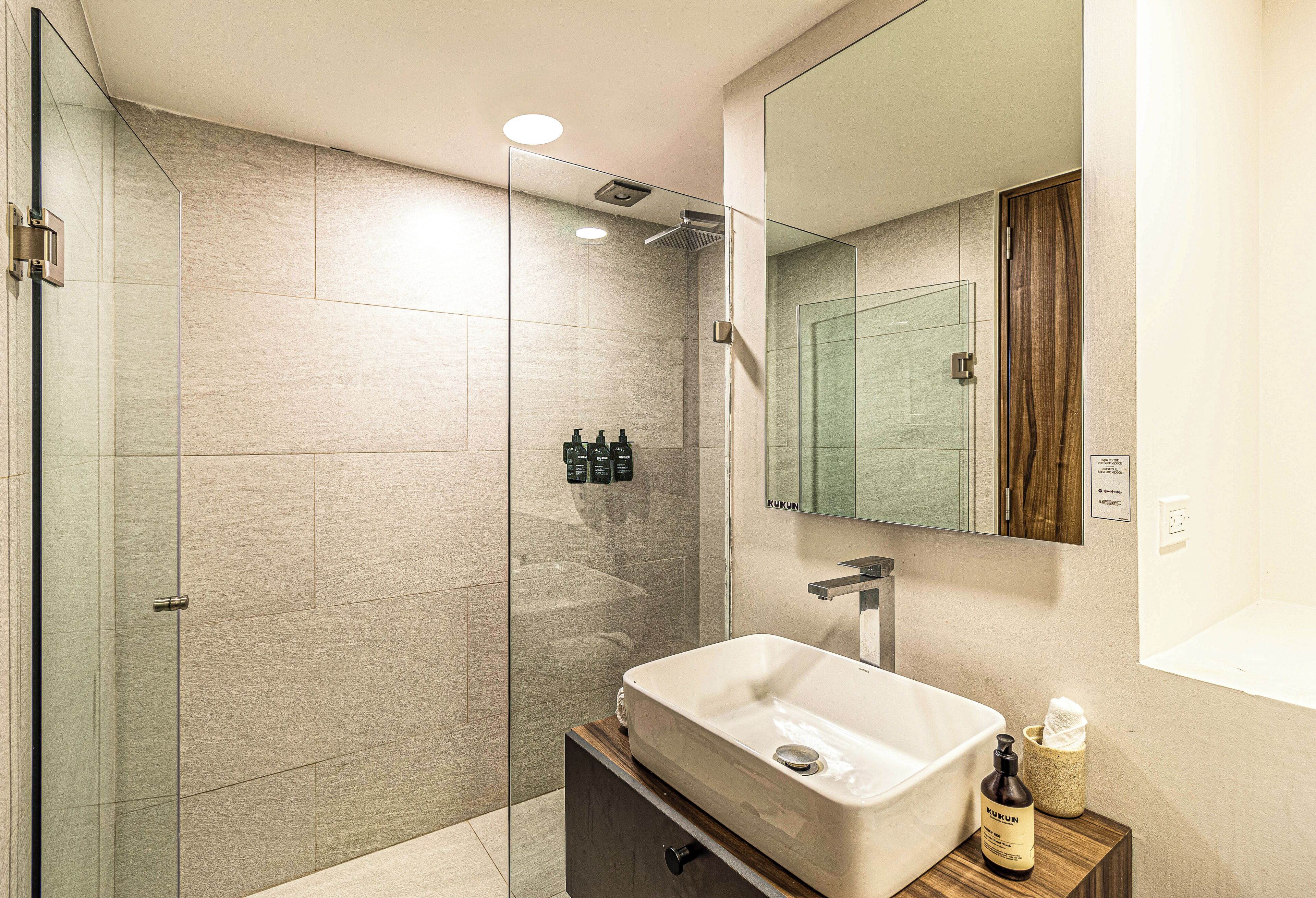 A modern bathroom with a glass shower enclosure, a large mirror, and a wooden vanity with a sink.