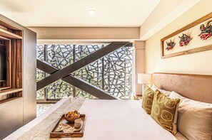 Un dormitorio con cama, almohadas, una bandeja con comida y una taza, una ventana con vistas y un adorno en la pared.