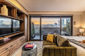 A modern living room with a flat-screen TV, a sofa, a coffee table, and a sliding glass door leading to an outdoor patio with chairs. - Kukun Tonalá 30 Roma (Mexico City)