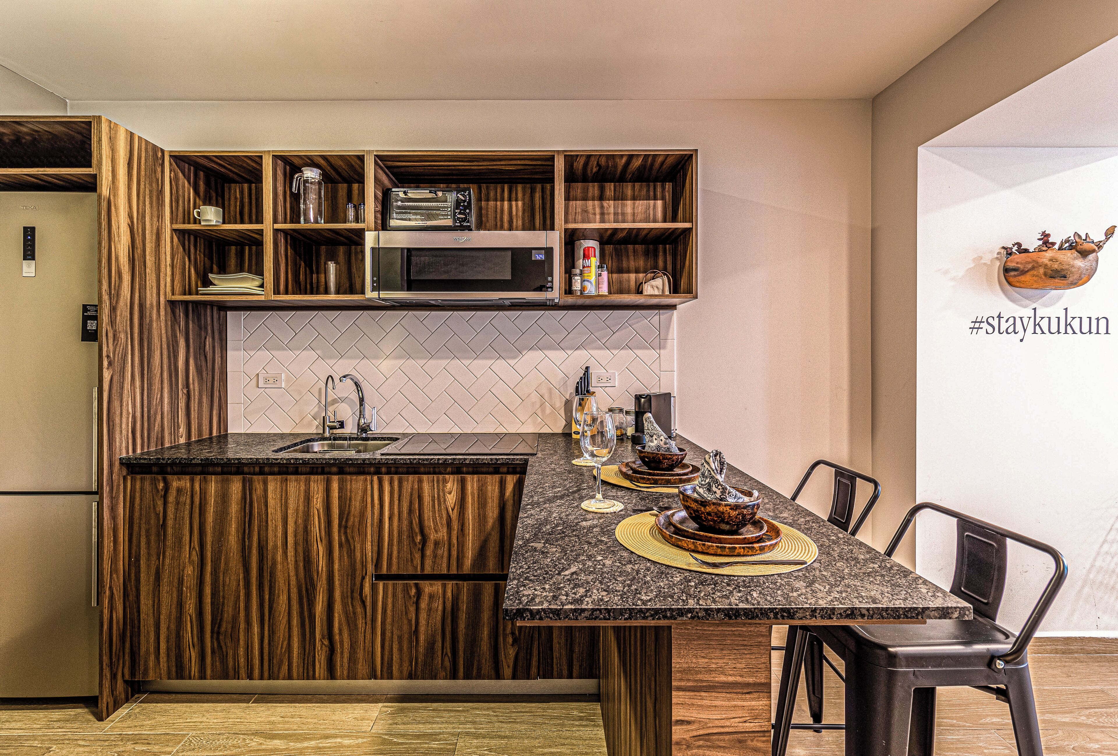 A kitchen with a central island, wooden cabinetry, a microwave, and a dining area with chairs.