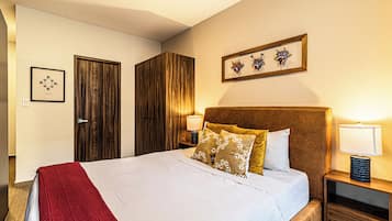 Quarto de hotel com uma cama, um guarda-roupa de madeira, uma mesa de cabeceira com abajur e um quadro na parede.