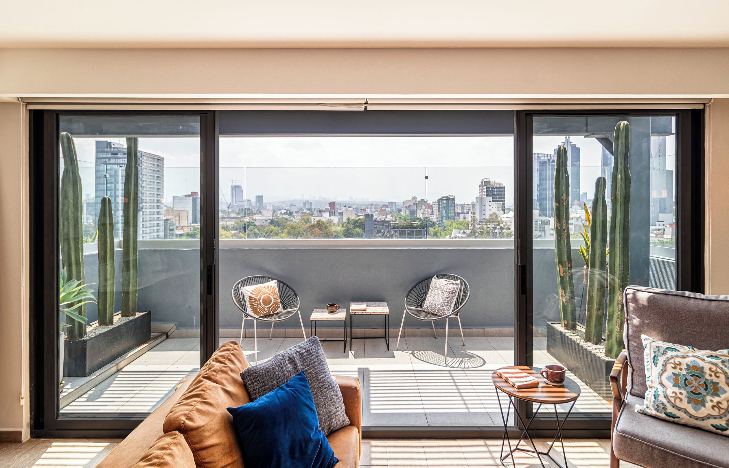 A balcony with a city view, two chairs, a sofa, and a small table with a cup and book.