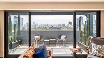 A balcony with a city view, two chairs, a sofa, and a small table with a cup and book.